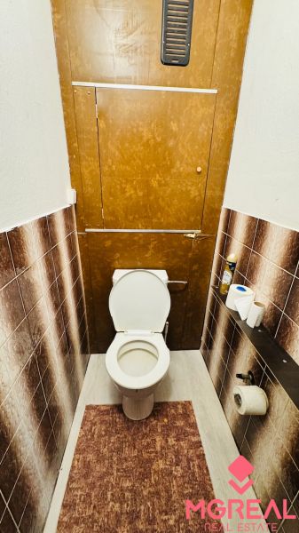 Háromszobás lakás WC-je barna csempékkel és lábtörlővel.