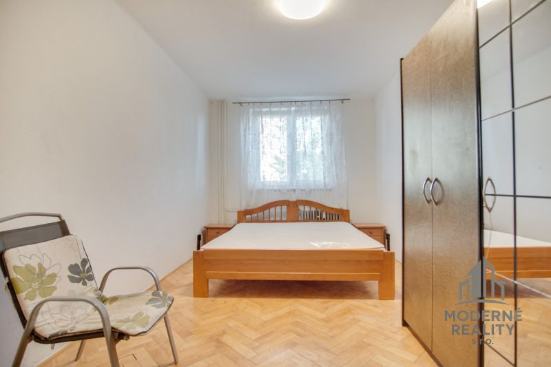 Hálószoba egy kétszobás lakásban franciaággyal, székkel és fa dekorációjú padlóval.