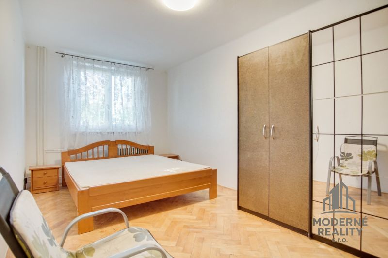 Hálószoba egy kétszobás lakásban fa mintázatú padlóval, ággyal és szekrénnyel.