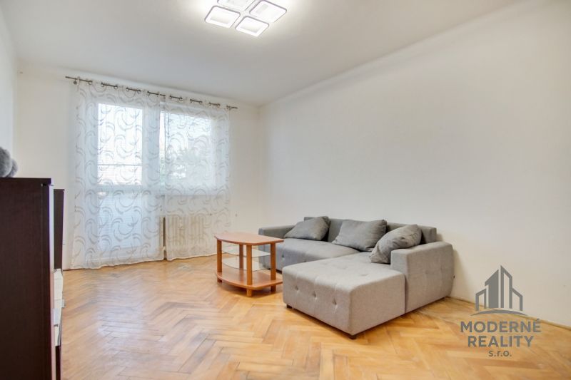 Nappali egy kétszobás lakásban, fa dekorációjú padlóval és szürke kanapéval.