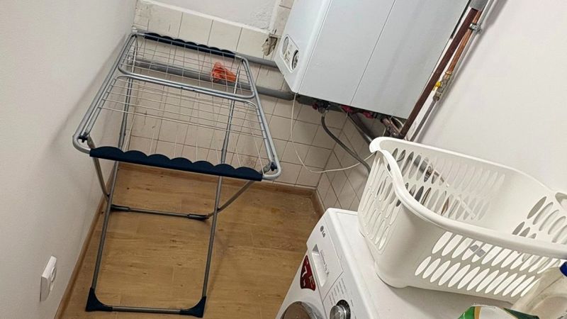 Mosókonyha családi házban mosógéppel, szárítóval és fa mintázatú padlóval.