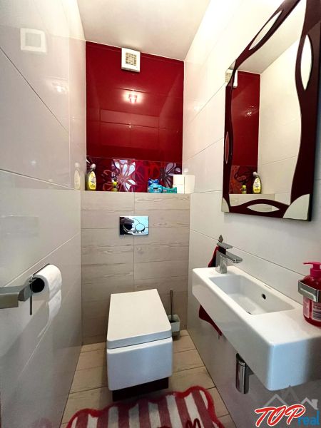 Fürdőszoba egy háromszobás lakásban függesztett WC-vel, mosdóval és piros csempékkel.