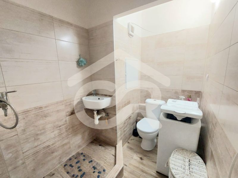 Fürdőszoba a garzonlakásban WC-vel, mosdóval és mosógéppel; fa hatású padlóval.