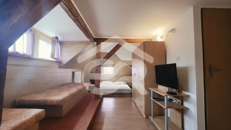 Nyaraló apartman belső tere ággyal, televízióval és fa dekorációjú padlóval.