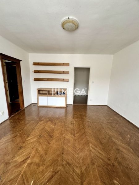 Szoba egy háromszobás lakásban, fa mintázatú padlóval és polcokkal a falon.