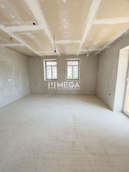 Tágas szoba egy családi házban nagy ablakokkal és betonpadlóval.