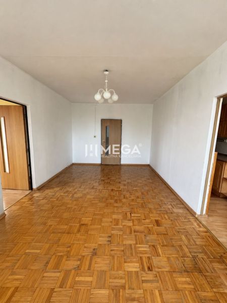 Nappali egy háromszobás lakásban, fa mintázatú padlóval és csillárral.