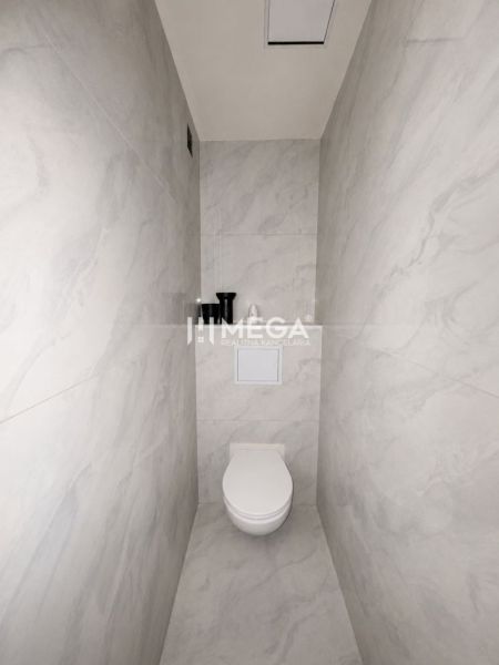 Minimalista dizájnnal és világos kerámia burkolattal rendelkező WC egy háromszobás lakásban.