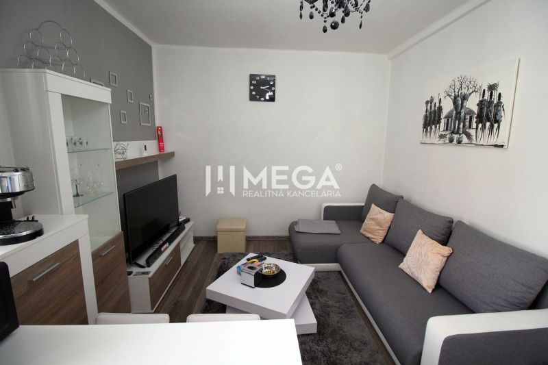 Nappali rekreációs apartman szürke kanapéval, TV-vel és fa dekor padlóval.