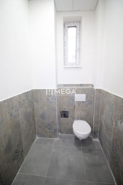 Egy egyszerűen kialakított, kereskedelmi helyiségben található fürdőszoba, amely WC-vel és keskeny ablakkal rendelkezik.