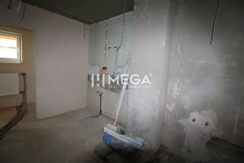 Befejezetlen belső tér egy családi házban betonpadlóval és radiátorcsatlakozással.