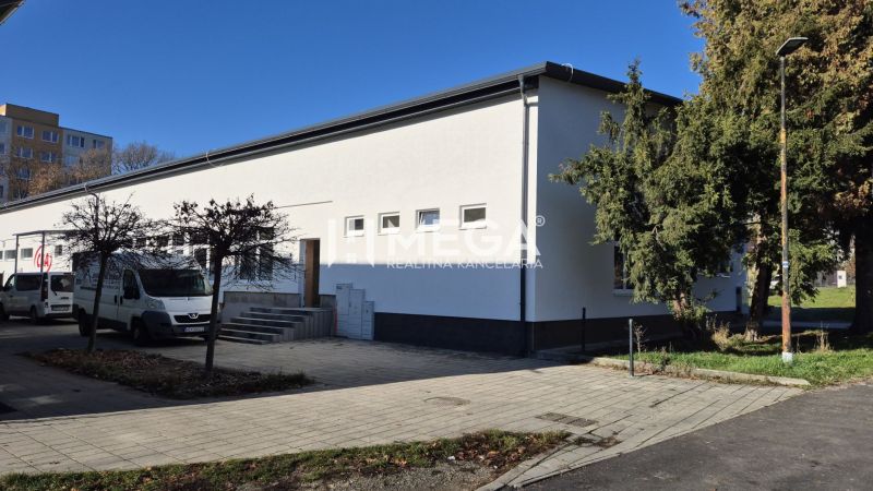 Üzlethelyiségek a Tyršová utcán Humennéban, fehér homlokzattal és körülötte fákkal.