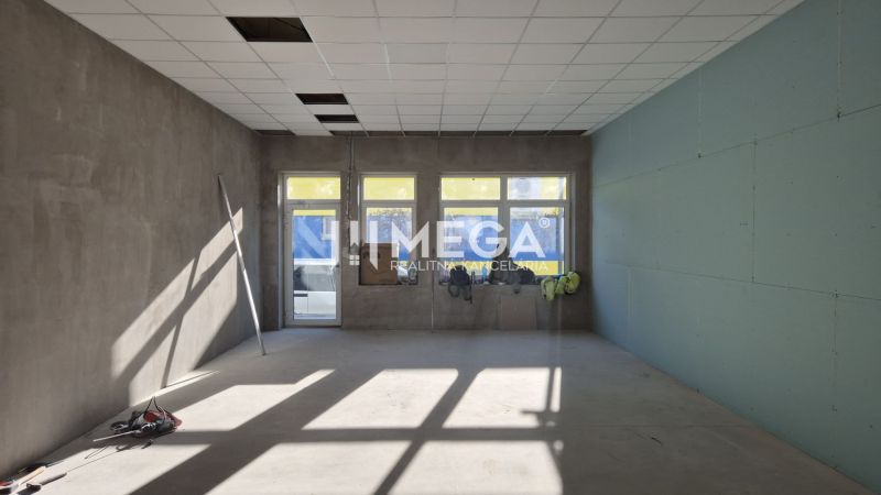 Kereskedelmi helyiségek magas ablakokkal, betonpadlóval és fehér mennyezettel.