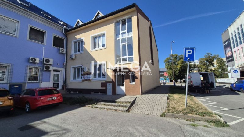 Üzlethelyiségeket tartalmazó épület a szabadság téren, Humennéban, amely előtt parkolóhelyek találhatók.