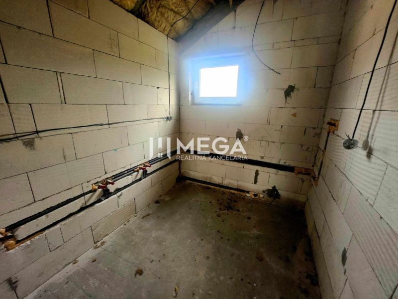 Családi ház belső tere betonpadlóval, téglafalakkal és kis ablakkal.