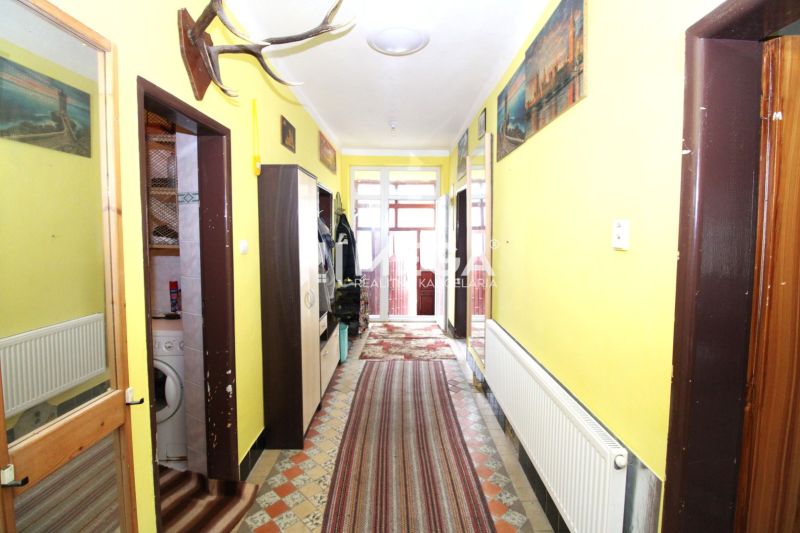 Egy családi ház folyosója radiátorral, szőnyegekkel és dekorációkkal a falakon.
