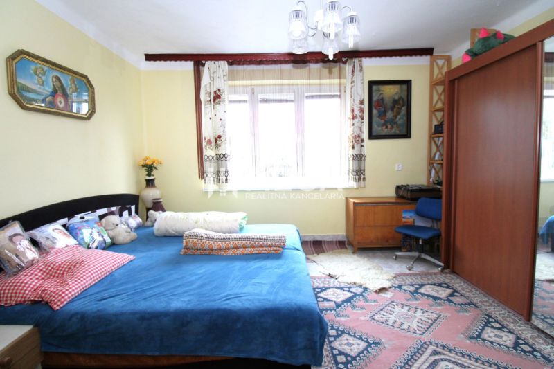 Hálószoba családi házban kék ággyal, fa bútorokkal és színes szőnyeggel.