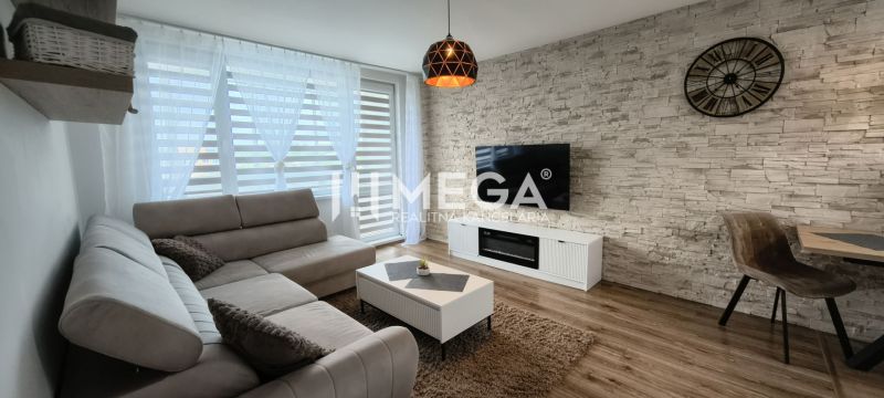 Nappali egy háromszobás lakásban, fa dekoros padlóval és kőfalra szerelt TV-vel.
