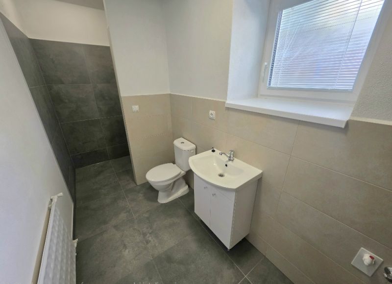 Fürdőszoba egy kétszobás lakásban WC-vel, mosdóval és zuhanyzóval zuhanyfüggöny nélkül.
