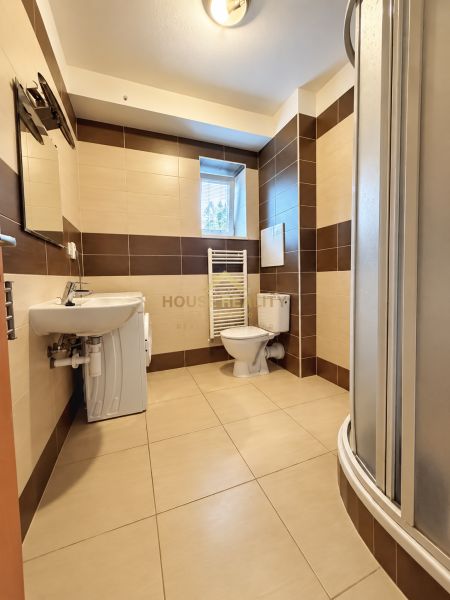 Fürdőszoba a garzonlakásban zuhanyzóval, mosógéppel, mosdóval és WC-vel.