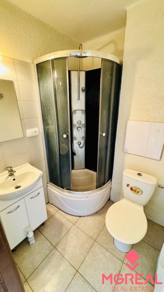 Fürdőszoba zuhanyzóval, mosdóval és WC-vel egy egyszobás lakásban.