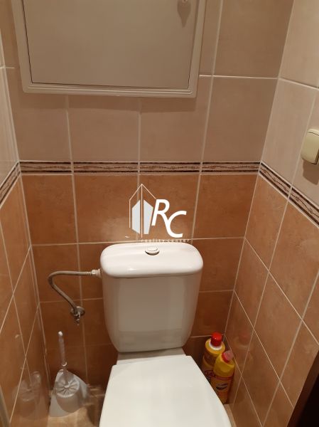 Fürdőszoba WC-vel egy kétszobás lakásban, világos csempék, tisztítószerek, öblítőtartály.
