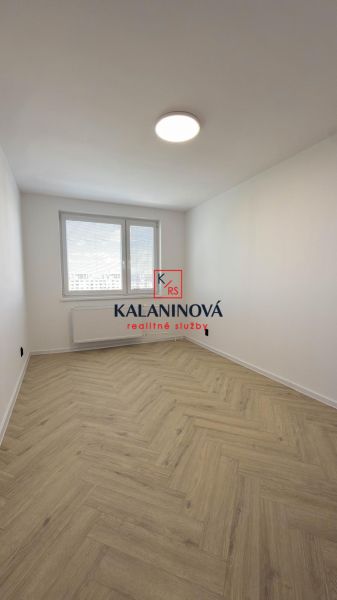 Egy négy szobás lakás fa dekoros padlóval rendelkező szobája elegánsan megvilágítva egy nagy ablakkal.