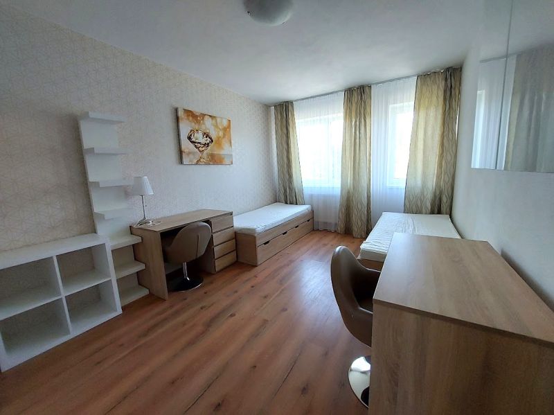 Szoba két ággyal, asztalokkal és fa dekorációjú padlóval egy háromszobás lakásban.