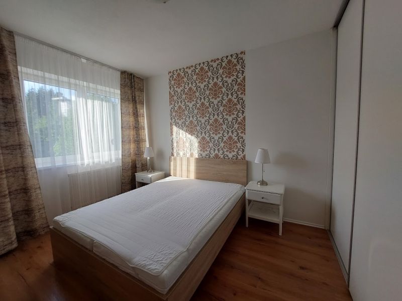 Hálószoba ággyal, tapétával és fa dekorációjú padlóval egy háromszobás lakásban.