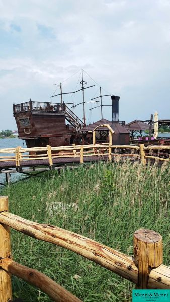 Fából készült hajó, mint látványosság a Senecké tavaknál lévő házikónál, fa kerítés mögött.