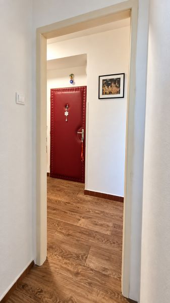 Folyosó piros ajtókkal és fa mintázatú padlóval egy háromszobás lakásban.
