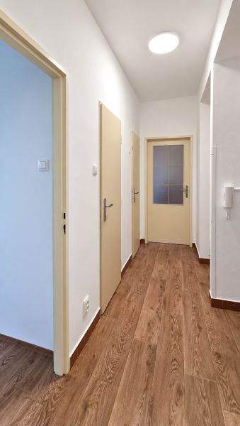 Folyosó három ajtóval és fa dekorációjú padlóval egy háromszobás lakásban.