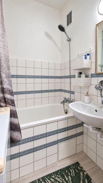 Fürdőszoba káddal, mosdóval, fehér csempével és mintás részletekkel egy háromszobás lakásban.