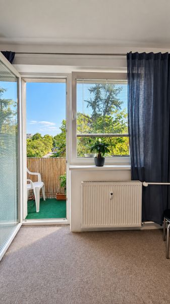 Nappali egy háromszobás lakásban, kilátással az erkélyre és a zöldövezetre.
