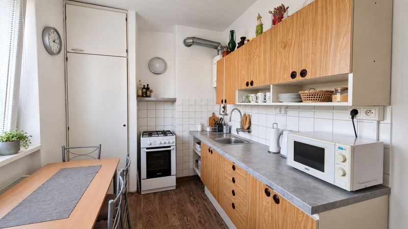 Konyha egy 3 szobás lakásban, konyhabútorral, háztartási gépekkel és fa mintázatú padlóval.