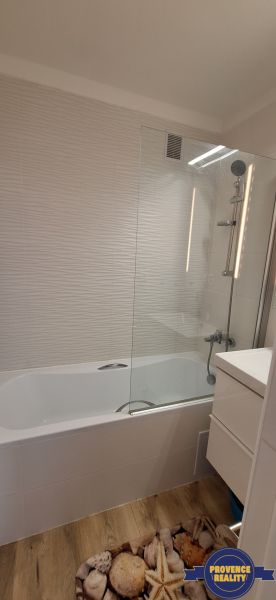 Fürdőszoba egy háromszobás lakásban, káddal, fehér csempékkel és fa dekoros padlóval.