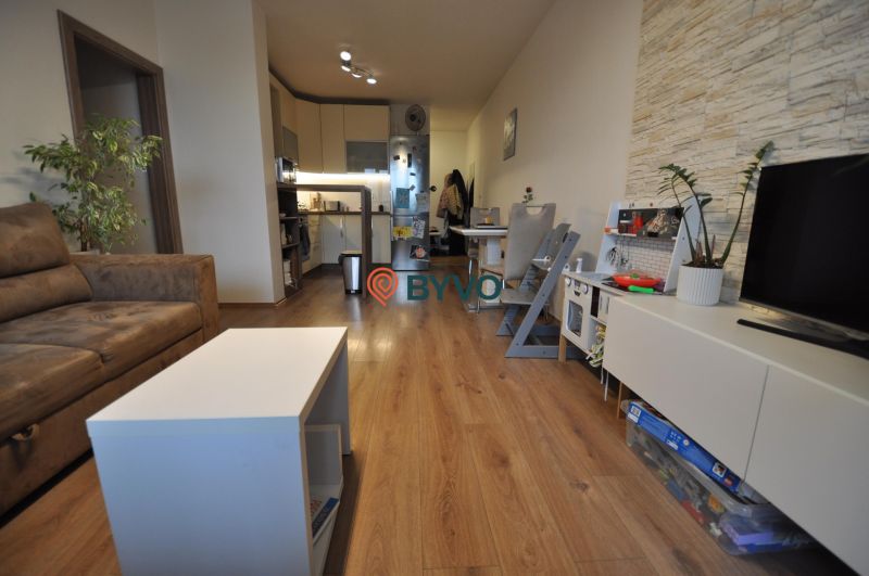 Nappali egy háromszobás lakásban fa dekor padlóval, ülőgarnitúrával és konyhával.