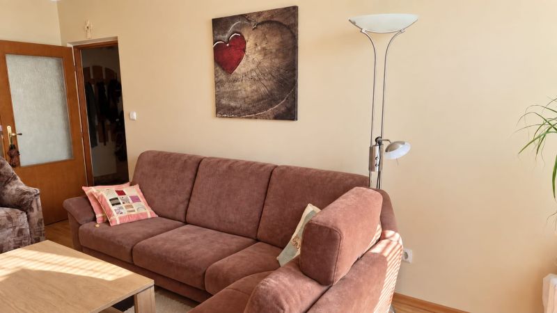Kényelmes nappali kanapéval, lámpával és művészeti képpel egy háromszobás lakásban.