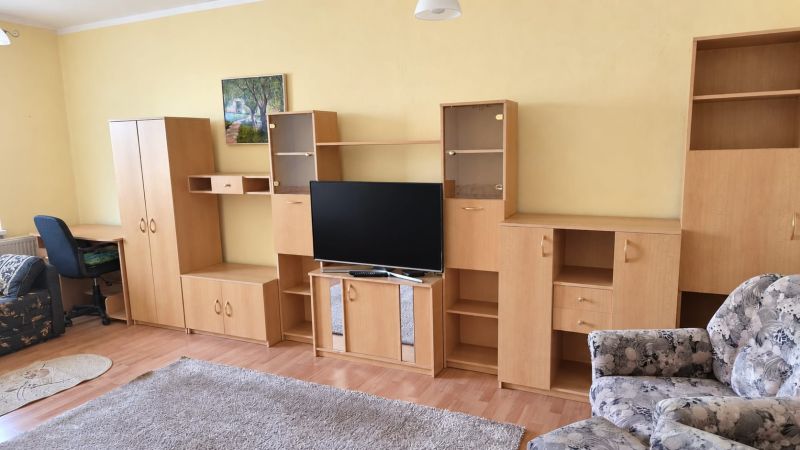 Nappali egy háromszobás lakásban, fa hatású padlóval, világos bútorokkal, televízióval.