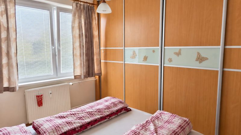 Hálószoba egy háromszobás lakásban beépített szekrénnyel és piros ágyneművel ellátott ággyal.