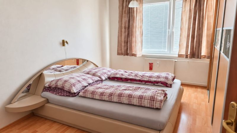 Hálószoba egy háromszobás lakásban, ággyal, tükör alatti szekrénnyel és fa dekoros padlóval.