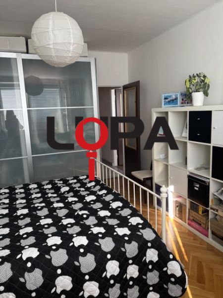 Hálószoba egy kétszobás lakásban tárolóhellyel, ággyal és fa dekoros padlóval.