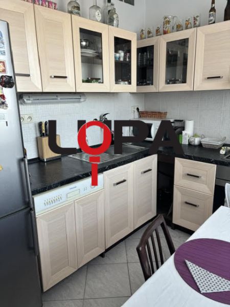 Konyha egy kétszobás lakásban fa dekorációjú bútorokkal és világos csempékkel.