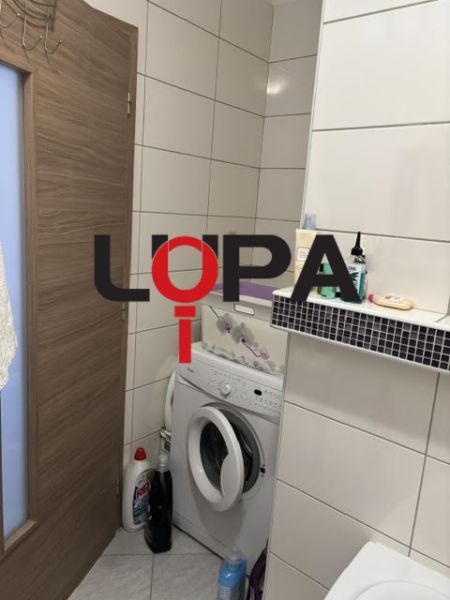 Fürdőszoba egy kétszobás lakásban mosógéppel és tárolóhellyel.