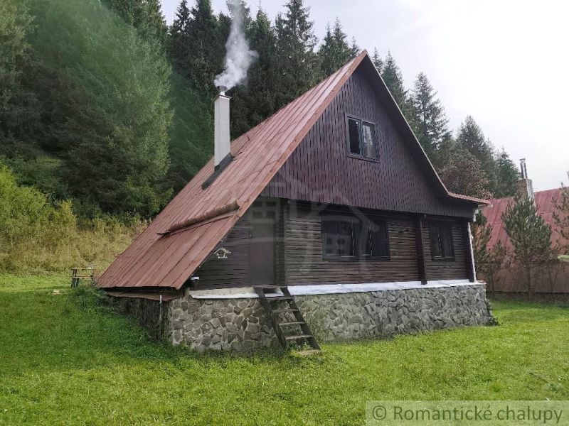 Házikó Rajecká Lesnában, erdővel körülvéve, füsttel a kéményből.