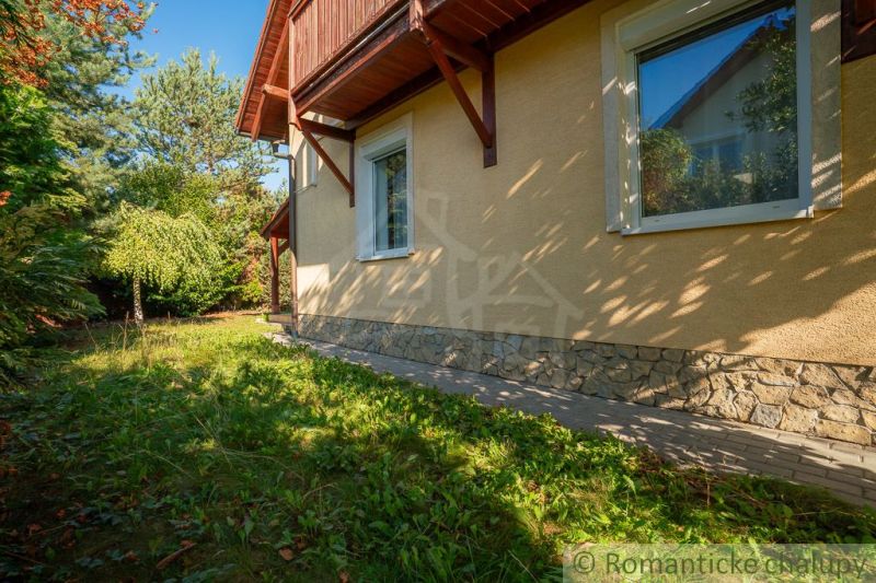 Családi ház Bernolákovóban kő lábazattal, zölddel és fákkal körülvéve.