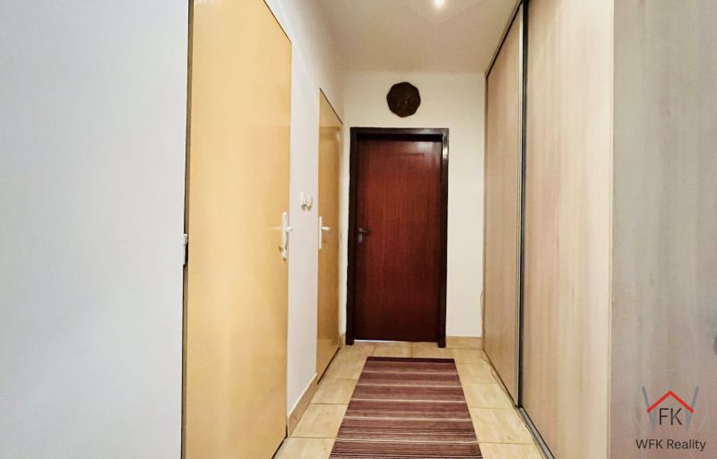 Folyosó egy 3 szobás lakásban tárolóhelyekkel és meleg tónusú szőnyeggel.