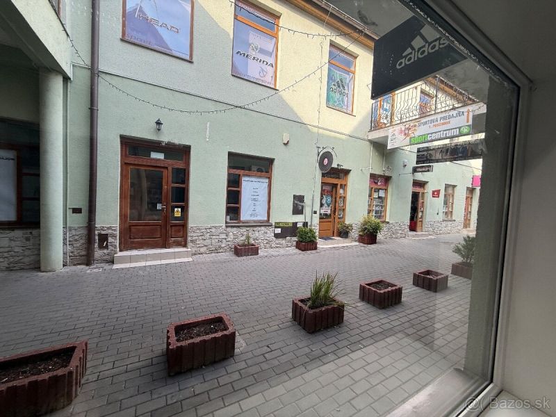 Üzlethelyiségek Nagytapolcsányban kőburkolattal és virágtartókkal a kövezett utcán.