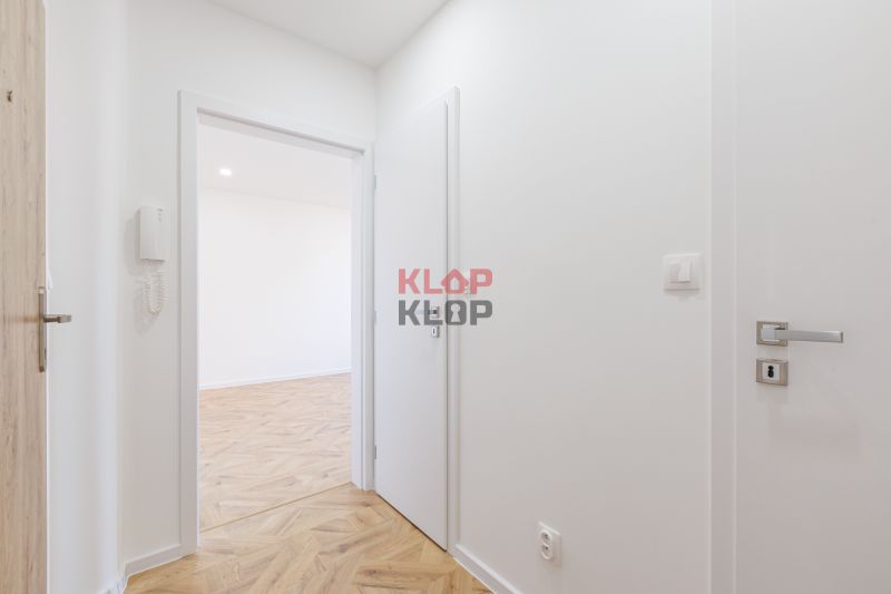 Folyosó egy kétszobás lakásban, fa mintázatú padlóval és fehér falakkal.