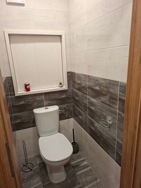 Fürdőszoba egy egyszobás lakásban WC-vel, sötétebb tónusú csempékkel burkolva.